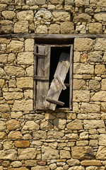 Old window with broken wooden shutter on a stone building