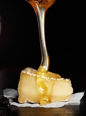 Slice of camembert with with honey (pouring from honey spoon).Black background