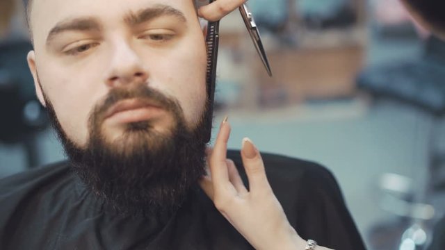 Female barber cuts the beard hair of the male client 4K
