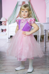 Little happy princess girl in pink dress and crown in her royal room posing and smiling. 
