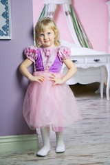 Little happy princess girl in pink dress and crown in her royal room posing and smiling. 
