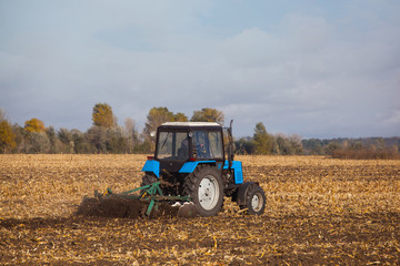 large blue tractor plow plowed land after harvesting the maize crop on a sunny clear autumn day. Part of the cultivator steel round discs in a row close-up. Work agricultural machines. Harvest.