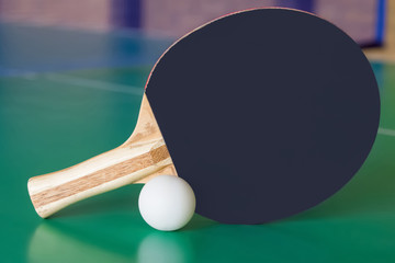 Black wooden racket for ping pong and white ball lying on the green table.