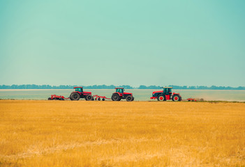 Obraz premium Summer day three tractors to plow plow the soil on sloping cornfield. Agricultural land treatment before planting.