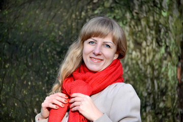 The joyful young woman ties a red scarf. A portrait against the