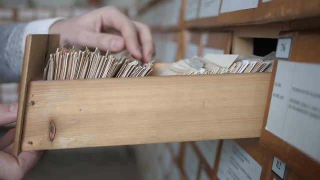 A hand opens a drawer and browse with fingers through the cards in the library card catalog