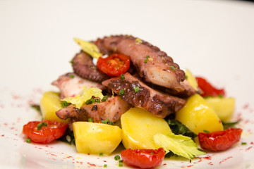 Potato salad with octopus and sun dried tomatoes lies on the pla