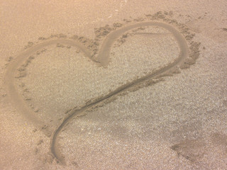 Fototapeta na wymiar Heart drawn in the sand. Beach background. Top view.
