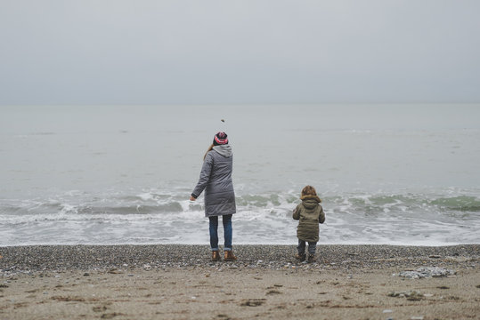 Мама и сын кидают камни в море зимой, зимнее море