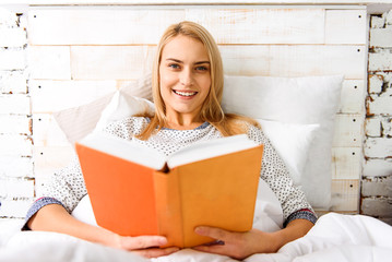 Carefree young woman reading literature in bedroom