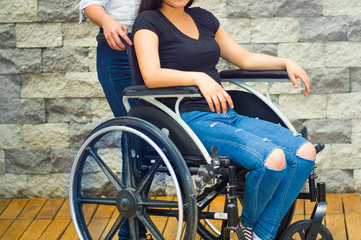 Young woman sitting in wheelchair with assistant standing next to her, both smiling happily showing...