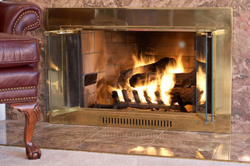 Old fashioned leather chair by a lit gas fireplace with marble hearth