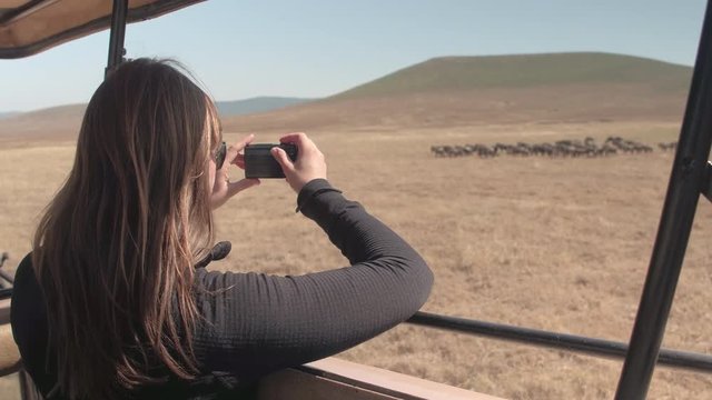 CLOSE UP: Girl on safari game ride in African savannah taking picture of animals