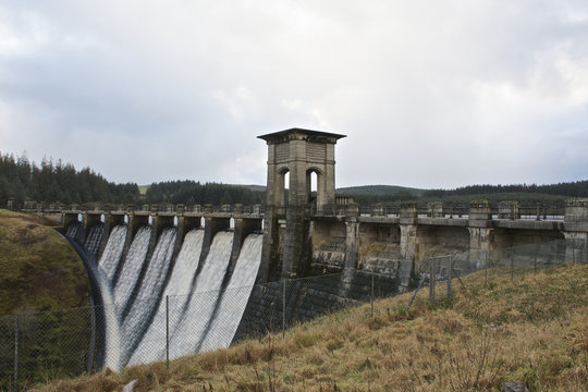 Alwen reservoir, Wales, UK winter day showing entire dam from the non lake side showing countryside around, water cascading down