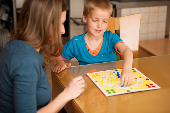 young boy plays ludo game with his mother on a table in livingro