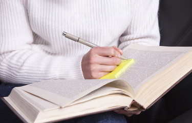 Girl with a book in hand taking notes with a pen.