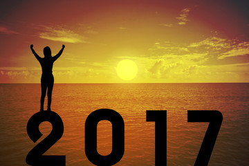 Silhouette young woman standing and raising up her hand about fighting concept on numbers 2017 over a beautiful sunset or sunrise at the sea, background for happy news years.