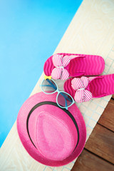 Pink hat, sunglasses and flip flops by   swimming pool