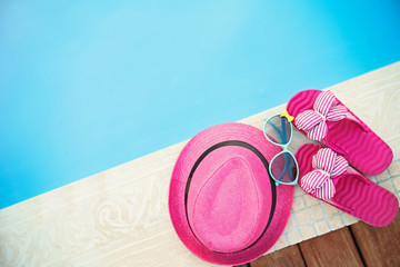 Pink hat, sunglasses and flip flops by   swimming pool