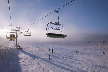 Winter mountains panorama with ski slopes and ski lifts, sunny day with fog and sun rays