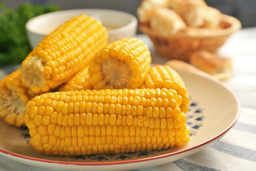 Plate with tasty boiled corncobs on kitchen table, close up view