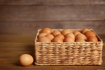 Raw eggs in basket on wooden background