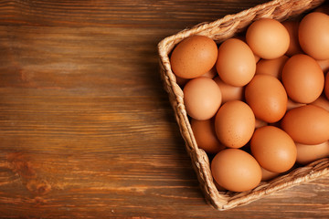 Raw eggs in basket on wooden background
