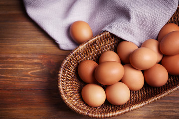 Raw eggs in basket on wooden background