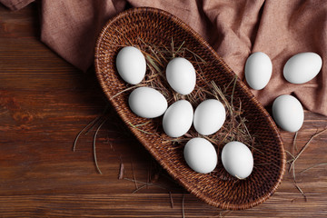Raw eggs in basket on wooden background