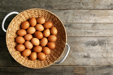Raw eggs in basket on wooden background