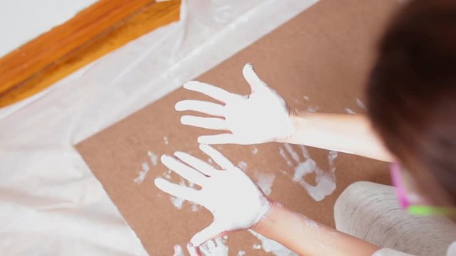 A little cute happy funny child painting white handprints with mother together