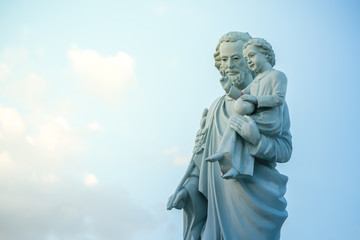 Fototapeta na wymiar classical statue of Saint Joseph with child Jesus on blue sky. Joseph is a figure in the Gospels, the husband of Mary, mother of Jesus and is venerated as Saint Joseph in the Catholic Church. 