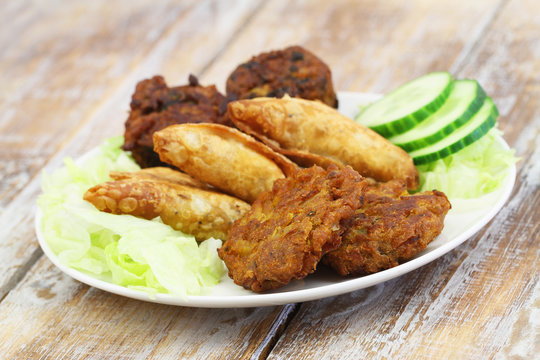 Indian snacks including samosas, onion bhajis and pakoras on white plate on wooden surface
