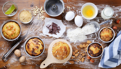 Muffins and baking cakes with cooking tools and ingredients: eggs, flour; brown sugar, pine nuts,...