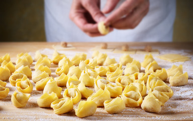 Man`s hands making tortellini on pastry board. - obrazy, fototapety, plakaty
