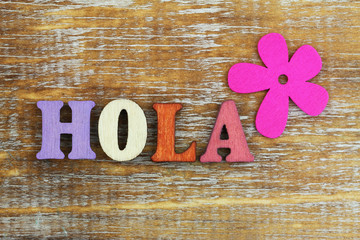 Hola (hello in Spanish) written with colorful wooden letters and pink flower   © graletta