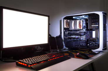 Custom built gaming computer with white screen, keyboard, mouse, desktop, components, hardware, gaming chair under low light. Selective focus. © daliu