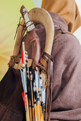 Medieval set of old wooden arrows with bright plumage in the quiver on human back in the cloak a hood