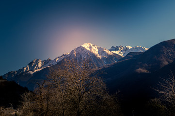 winter landscape in a sunny day, trees on foreground, snow-covered mountains on background