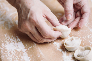 Close up view of woman folds the raw dumplings on a sheet of parchment