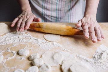 Image of two woman's hands making meat dumpling with wooden rolling pin.