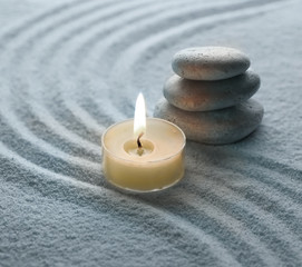 Fototapeta na wymiar light warm candle and stone on sand