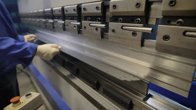 Worker in factory at metal skip machine putting work piece in. Man working with sheet metal and special machine tools for bending. Modern machines can accurately perform tasks.