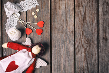 Angel a soft toy with heart, lace ribbon, buttons and three red hearts on old wood background. Valentine concept. Top view.