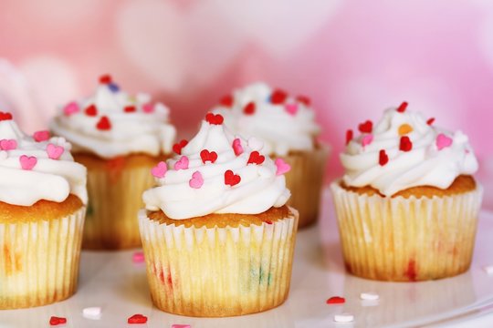 Homemade Valentine cupcakes topped with heart shaped sprinkles on Pink background,selective focus