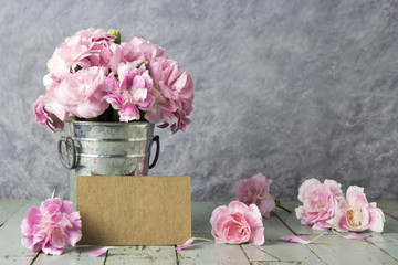 Pink carnation flowers in zinc bucket and blank brown card