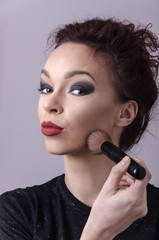 Beautiful young girl holding a makeup brush and blending face