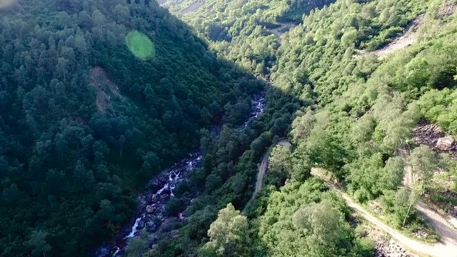 ripresa aerea panoramica tra gole delle montagne sopra al torrente con acqua che scorre, piante verdi e rocce sullo sfondo in una bellissima giornata soleggiata