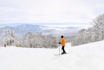 Fototapeta na wymiar Skier taking in the beautiful Myoko scenery before continuing down the mountain. Distant mountain ranges are partially covered by low lying clouds.