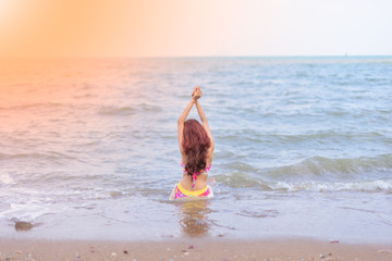 girl wearing a bikini sitting on a deserted tropical beach at su